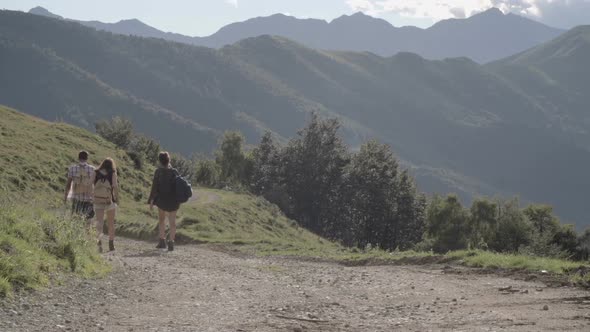 Young Friends Hiking Away on a Road in Mountain Outdoor Nature Scenery During Summer Sunrise or