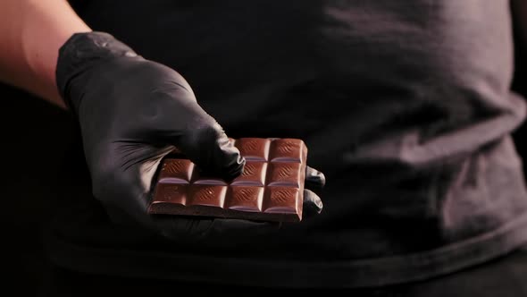 Chef Chocolatier in Black Gloves Breaks Chocolate Bar in Half for Melting and Making Sweets Cooking