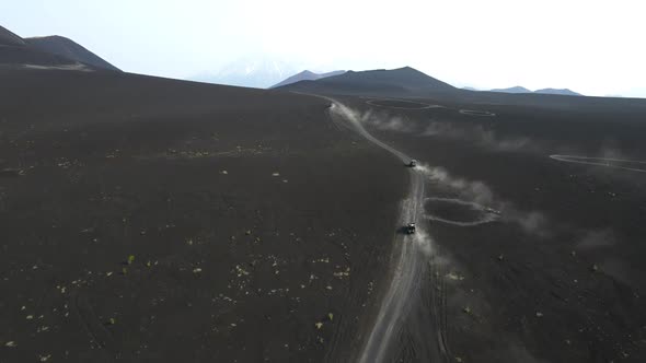 cars drive on black earth overlooking volcanoes