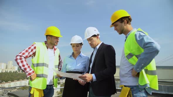 Architects Discussing Building Plan With Construction Workers Standing Roof