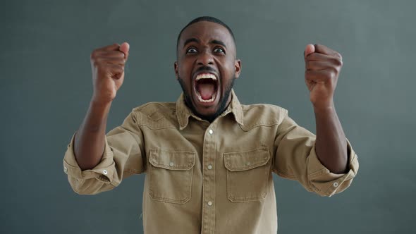 Portrait of Joyful African American Person Laughing and Raising Arms on Gray Background