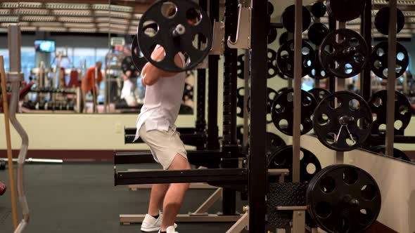 Side shot of bodybuilder doing barbell squats with heavy barbell with weights.