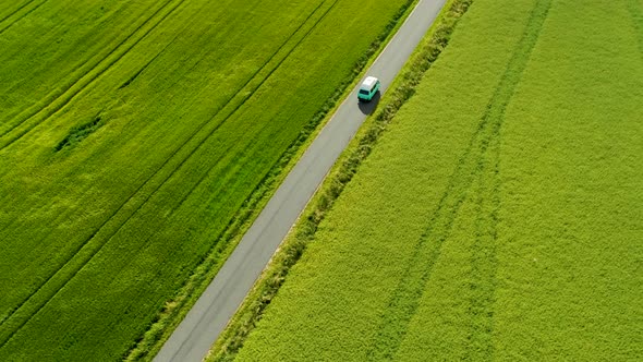 Mini Bus Driving On Narrow Country Road, With Green Fields On Both Sides, Drone Stock Footage 2x New