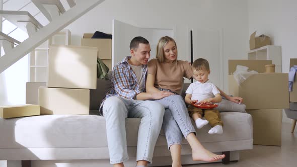 Happy Family Householders with Kid Sitting on Couch at New Home at Moving Day