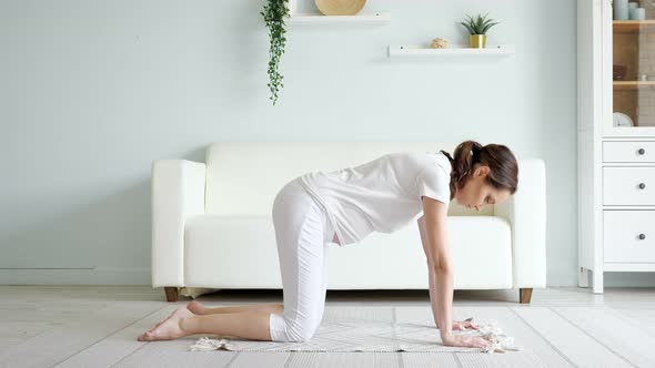 Pregnant Lady Does Marjaryasana on Floor Near Sofa at Home