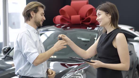 Side View of Smiling Woman Passing Car Keys To Happy New Owner in Dealership, Positive Caucasian
