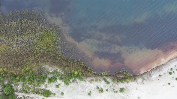 Aerial view at a beach with white sand and slow moving waves on the natural water with a clear view