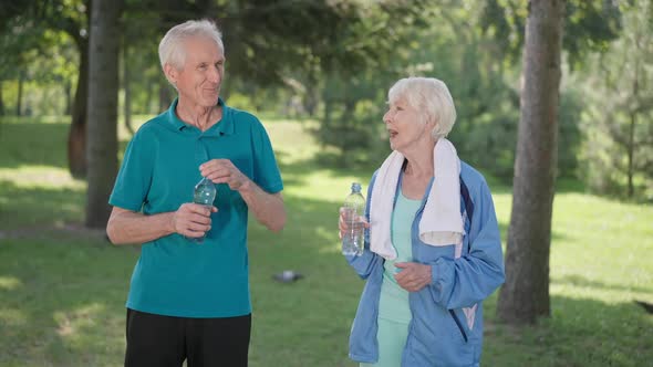 Positive Senior Sportive Couple Talking After Training Outdoors Drinking Refreshing Water in Slow