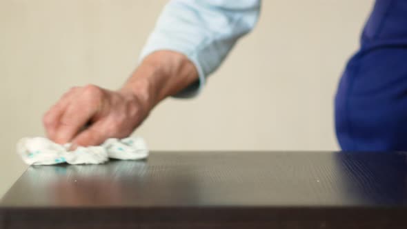 Active pensioner cleans the house, wipes dust with a rag from home furniture. Hands of an elderly pe