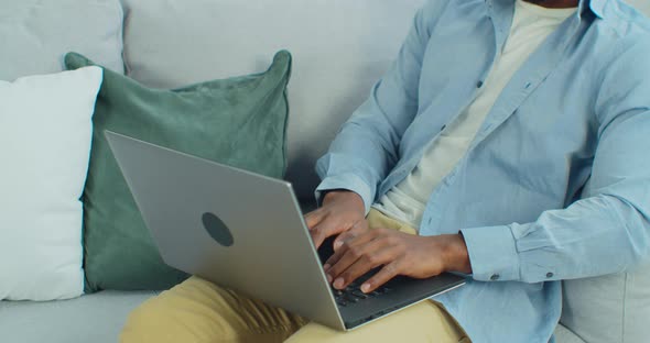 Close Up Hands of AfricanAmerican Man Uses Laptop Computer While Sitting on Sofa at Home