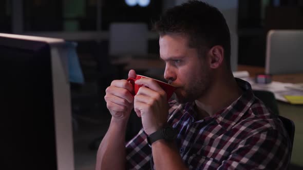 Businessman drinking coffee and working in a modern office by night