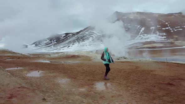 Woman walking on geothermal field with fumaroles and geysers. Area with natural steam vents and mud