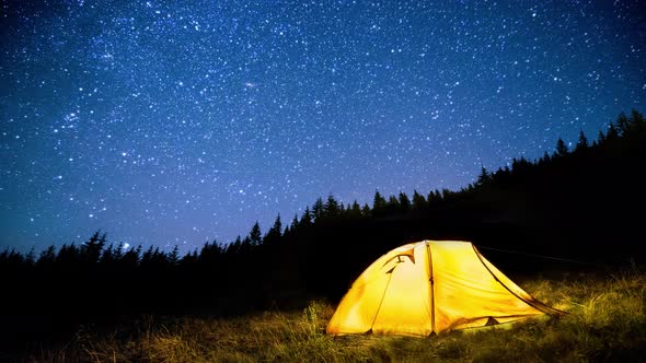 Glowing camping tent in the night mountain forest under the twinkling starry sky. Cinemagraph.