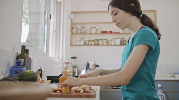 Teenage girl working cutting fruit for breakfast in the kitchen