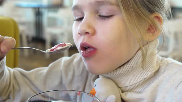 a Little Girl with a Sweater with a Toy Eats Ice Cream with Syrup