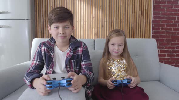 Two Caucasian Children Playing Video Game As Sitting on Couch at Home. Boy and Girl Winning, Making