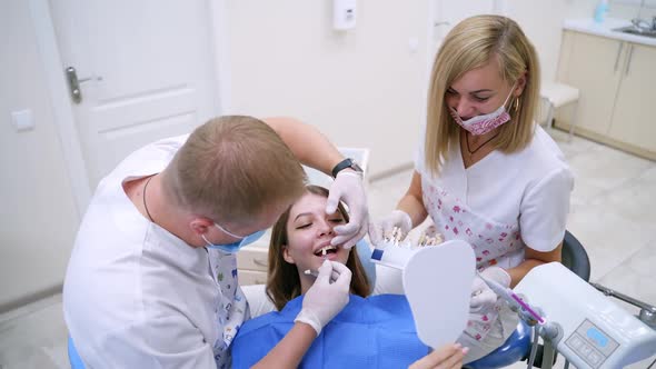 Stomatologist selecting tooth implant for female patient in modern dentist office.