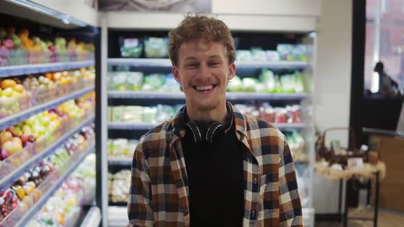 Close Up of the Handsome Young Caucasian Guy with Headphones Doing Shopping in the Supermarket and