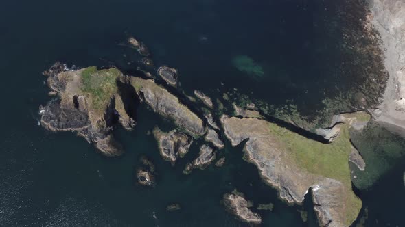 Ocean aerial ascends slowly from rugged steep rock islets near shore