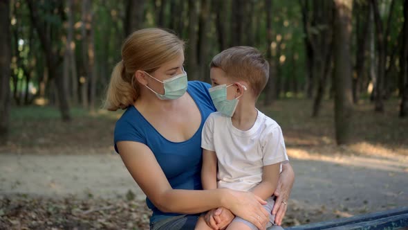 Mother Hugs Her Son in Medical Masks While Sitting in a Park