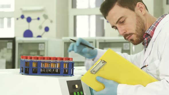 A Young Laboratory Assistant Takes Out Test Tubes with Analyzes and Rewrites Data About Them