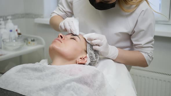 Doctor Beautician in a Black Mask Makes Cleaning the Face of a Young Woman