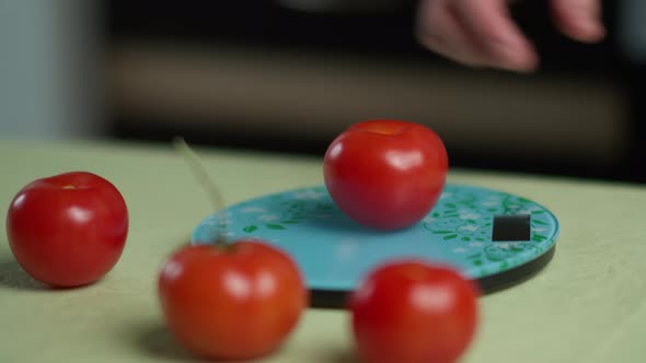 A Man Weighs Several Ripe Tomatoes on a Kitchen Scale