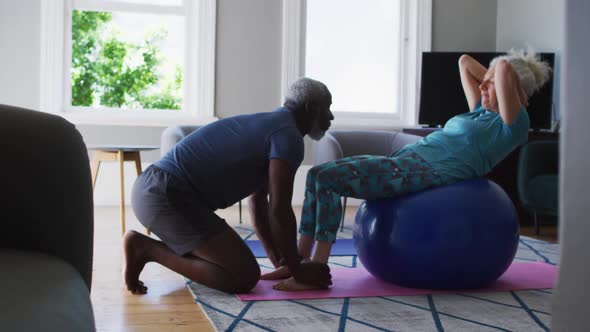 Mixed race senior couple performing exercise together in the living room at home