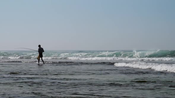 Local Fisherman Holds Rod in Hand in Waving Blue Ocean