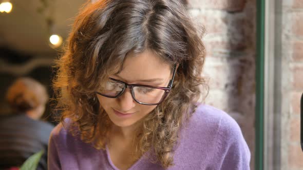 Young Woman Takes Notes in Pad Sitting on Cafe Windowsill