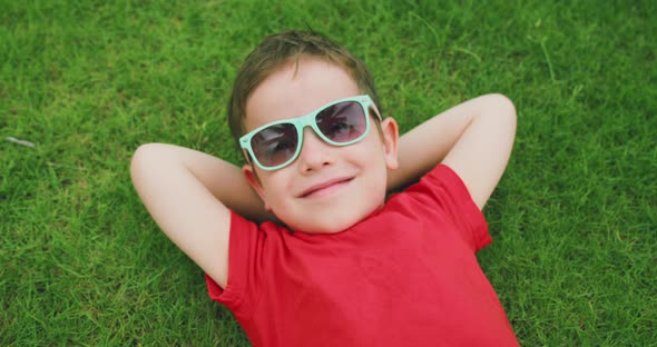 Happy Cute Child Lies on the Green Grass a Little Boy in Sunglasses Lies on the Grass Resting