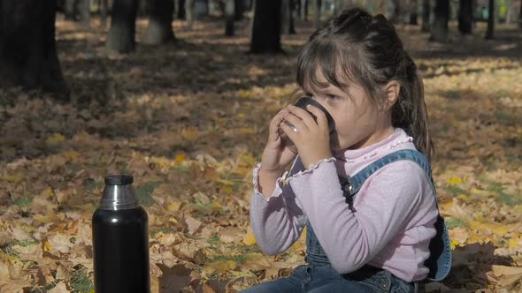 A Child Drinks a Hot Drink in Nature