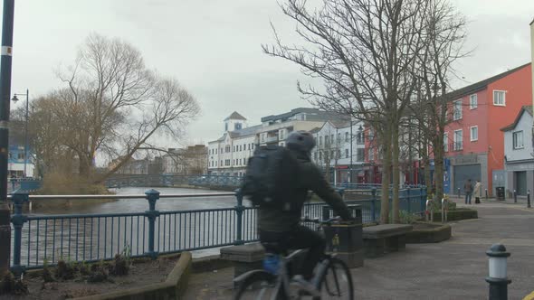 Male cyclist cycling by the riverside in city. STATIC WIDE SHOT