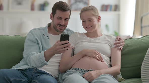 Pregnant Couple Browsing Smartphone at Home