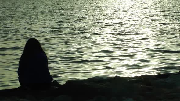 Woman Sitting On Rock On Beach At Sunset