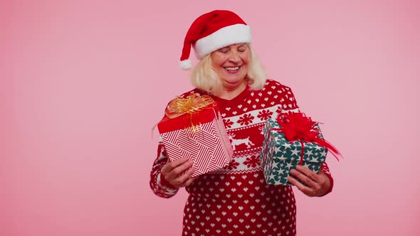 Grandmother in Santa Sweater Presenting One Christmas Gift Box Stretches Out His Hands to Camera