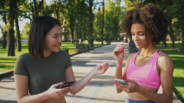 Two Multiethnic Female Friends Sharing Earbuds to Listen Music in Park Tracking Shot
