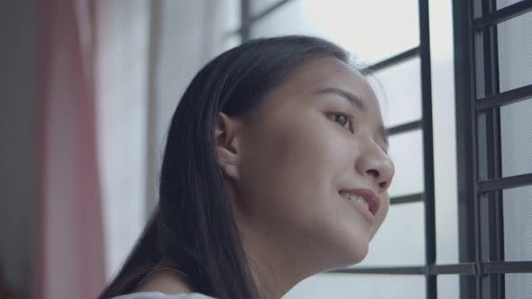 Close-up portrait smiling Asian woman opening curtains in the room at home.