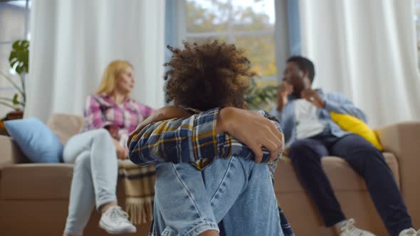 African Son Crying While Multiethnic Parents Having Quarrel Sitting on Couch at Background