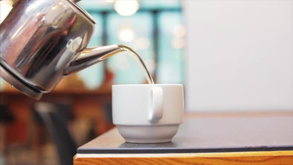 A Woman's Hand Pours Tea From a Chrome Teapot Slowly Poured Into a White Porcelain Cup