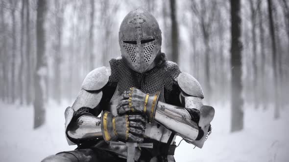 Portrait of Medieval Knight in Helmet Holding Steel Sword and Kneeling on Winter Nature in Slow
