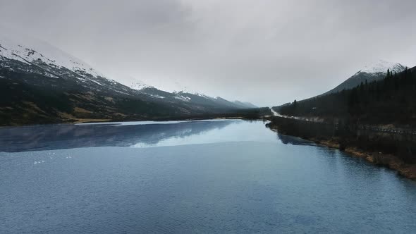 River with flock of trumpeter swans between the mountains with the road in Summit Lake, Alaska, USA