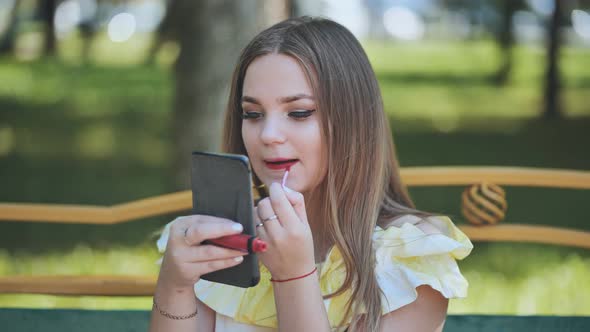 A Girl Paints Her Lips in the Park in the Summer