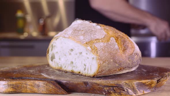 Sourdough Bread Loaf On A Kitchen Table With Man Walking In Blurry Background - close up, slider sho