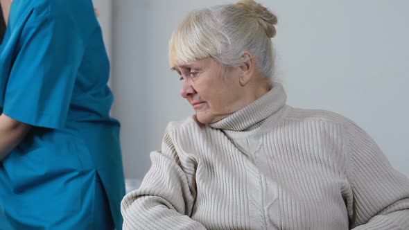 Medical Worker Moving Aside Sad Disabled Aged Female in Wheelchair, Loneliness