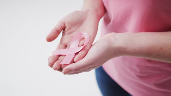 Mid section of woman holding a pink ribbon against white background