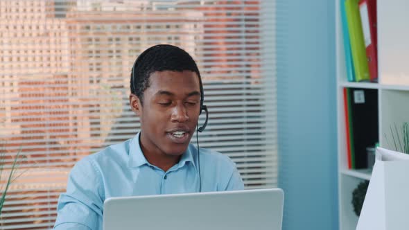 Close-up of Black Man in Headset Speaking with Somebody and Working on the Computer.