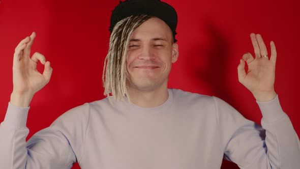 Young Handsome Smiling Man in Black Cap Meditating Looking at Camera on Red Background in Studio