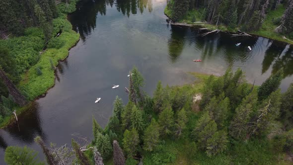 Counterclockwise drone shot of paddleboarders and kayakers coming around a bend in the Payette River