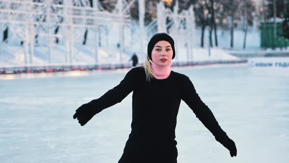 Young Beautiful Woman Training Her Figure Skating on Public Ice Rink and Looking in the Camera